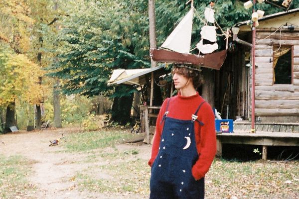 Musician Cosmo Sheldrake standing in a forest wearing a boat hat