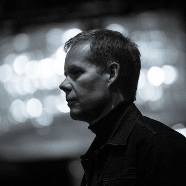 A monochrome shot of Max Richter standing looking to the left.