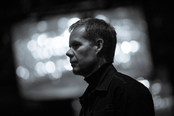 A monochrome shot of Max Richter standing looking to the left.